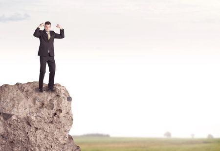 A successful good looking business person standing on top of a high cliff above country landscape with clear white sky concept
