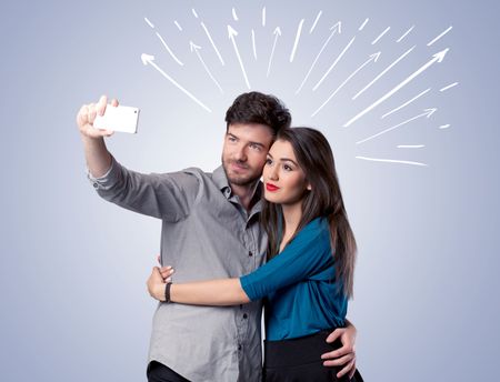 A cheerful young couple taking selfie photo with mobile phone and white lines and arrows pointing to the sky above them concept