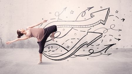 A beautiful young hip hop dancer dancing contemporary street dance in front of urban grey wall background with lines and arrows concept