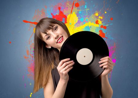 Young lady holding vinyl record on a grey background with colorful splashes behind her