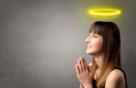 Young woman praying on a grey background with a shiny yellow halo above her head