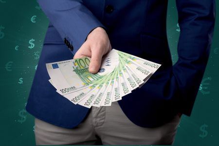 Young businessman holding large amount of bills with green background and currency symbols 