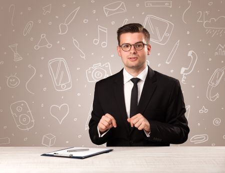 Young handsome businessman sitting at a desk with white mixed media icons behind him