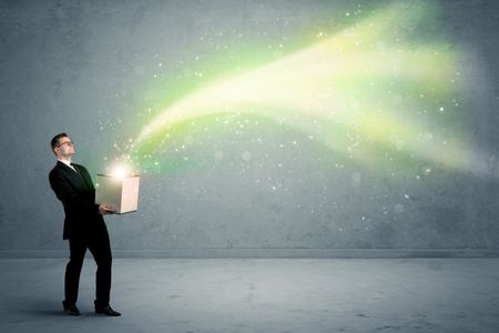 Bright yellow, green light beams escaping a cardboard box held by young elegant male business person in stylish suit concept.