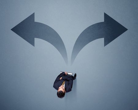 Young smart businessman standing in front of two arrows potinting to different ways contemplating a decision 