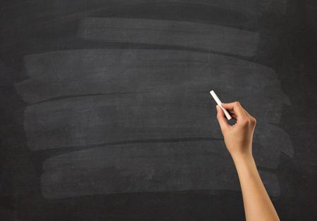 Female hand holding white chalk in front of a blank blackboard