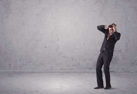 A surprised young sales person in elegant suit standing in empty urban environment with grey concrete wall background concept