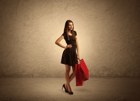 A beautiful young girl standing with red shopping bags in front of clear empty sepia urban wall background concept