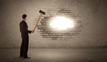 Business man hitting brick grungy wall with hammer and opening a hole
