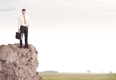 A successful good looking business person standing on top of a high cliff above country landscape with clear white sky concept