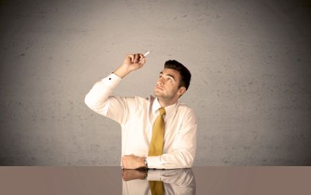 A happy businessman sitting at desk in front of clear grey empty background and drawing around himself with a white chalk concept