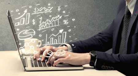 Sales person in suit using a laptop to calculate pie chart and exponential growth statistics on office desk concept