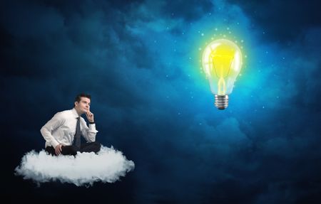 Caucasian businessman sitting on a white fluffy cloud lookind and wondering at a big, shiny, glowing yellow lightbulb