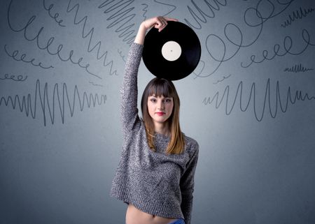 Young lady holding vinyl record on a grey background with scribbles around her