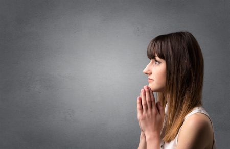 Young woman praying on a grey background