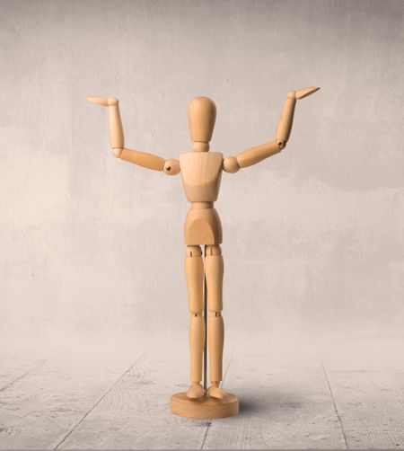 Wooden mannequin posed in front of a greyish background