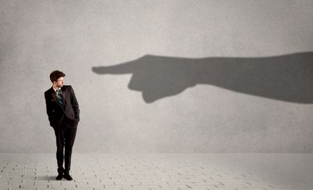 Business person looking at huge shadow hand pointing at him concept on background