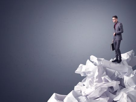 Thoughtful young businessman standing on a pile of crumpled paper with a dark grey background