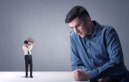Young professional businessman being angry with an other miniature businessman in front of a blueish grey background