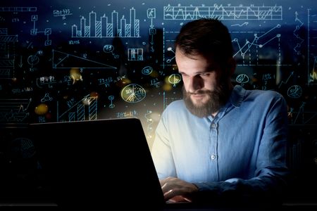 Young handsome businessman working late at night in the office with blue calculations in the background