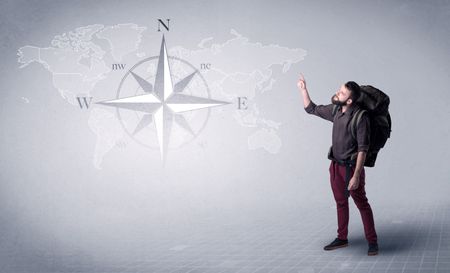 Handsome young man standing with a backpack on his back and a compass and a world map in the background