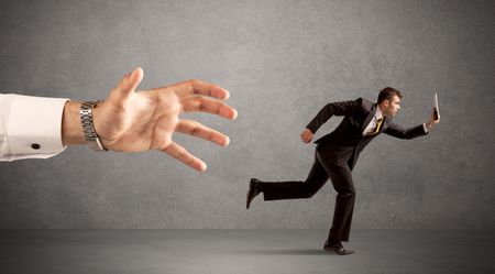 Young miniature businessman running from a big hand with light grey background