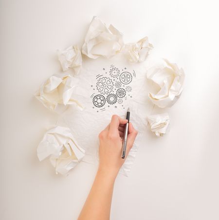 Female hand next to a few crumpled paper balls drawing rotating gears