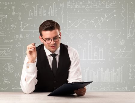 Young handsome businessman sitting at a desk with white graphs and calculations behind him 
