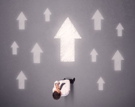 Young contemplating businessman stands in front of white arrows