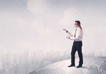 Young blindfolded businessman steps on a grey world map with a city in the background