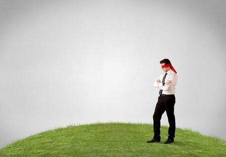 Young blindfolded businessman steps on a patch of grass