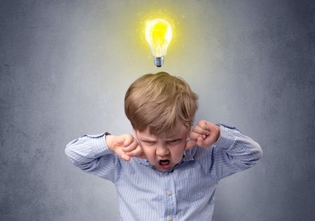 Adorable little kid mull over in front of a grey wall with idea symbol above his head