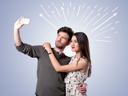 A cheerful young couple taking selfie photo with mobile phone and white lines and arrows pointing to the sky above them concept