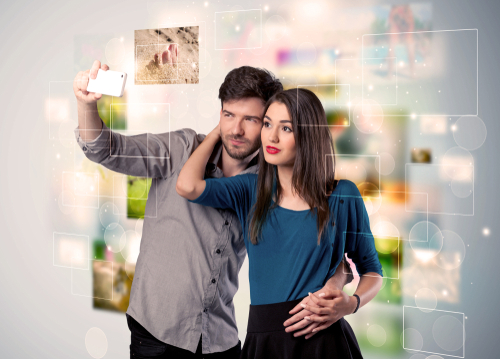 Collecting memories concept with photos in backbround and a happy young couple in love taking selfie with a mobile phone