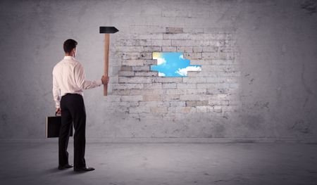 Business man hitting grungy brick wall with hammer