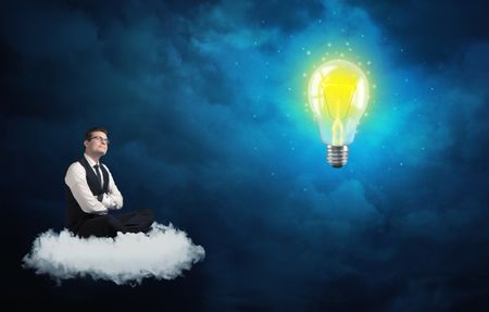 Caucasian businessman sitting on a white fluffy cloud lookind and wondering at a big, shiny, glowing yellow lightbulb