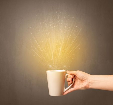 Young female hand holding tea mug with a beam of light rising out of it