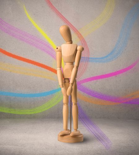 Wooden mannequin posed in front of a greyish background with colorful lines behind it