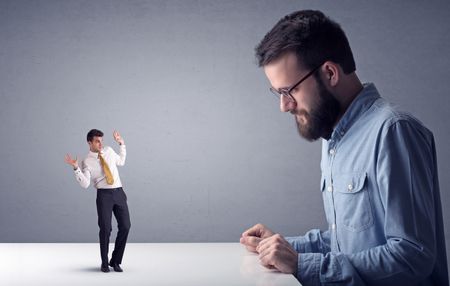Young professional businessman being angry with an other miniature businessman in front of a grey background