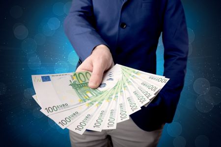 Young businessman holding large amount of bills with shiny blue background