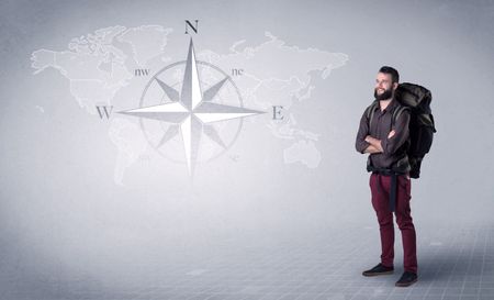 Handsome young man standing with a backpack on his back and a compass and a world map in the background