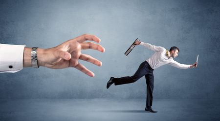 Young miniature businessman running from a big hand 