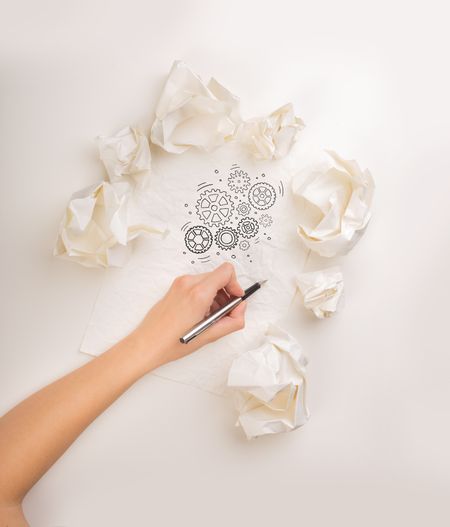 Female hand next to a few crumpled paper balls drawing rotating gears