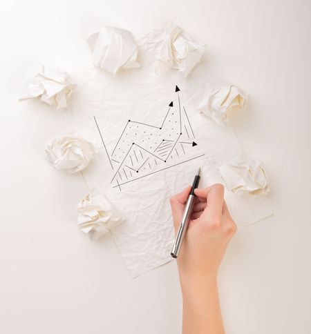 Female hand next to a few crumpled paper balls drawing a progress chart