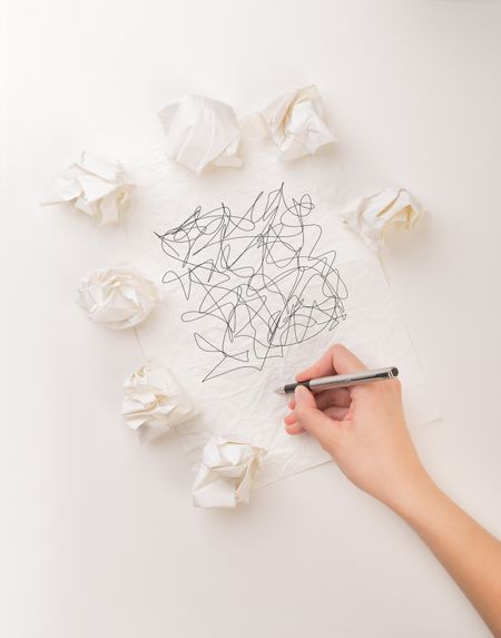 Female hand next to a few crumpled paper balls drawing random scribbles 