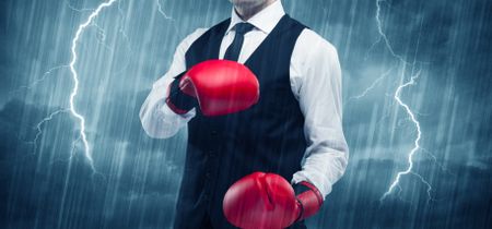 A dangerous sales person getting ready for a fight concept with red boxing gloves and thunder lightning in background.