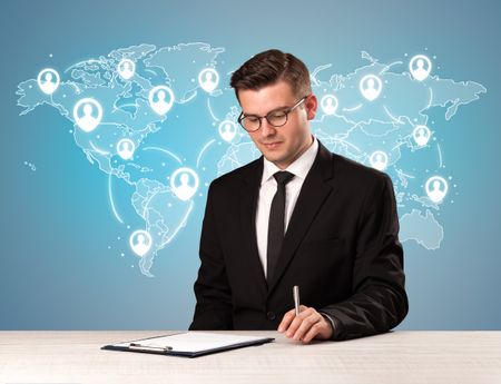 Young handsome businessman sitting at a desk with a blue world map behind him