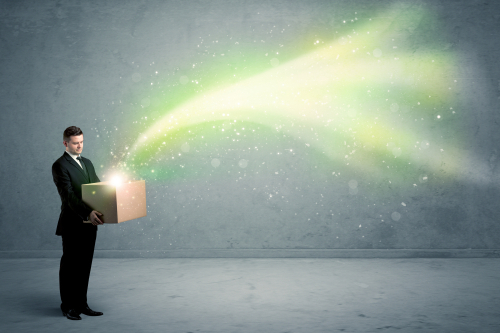 Bright yellow, green light beams escaping a cardboard box held by young elegant male business person in stylish suit concept.