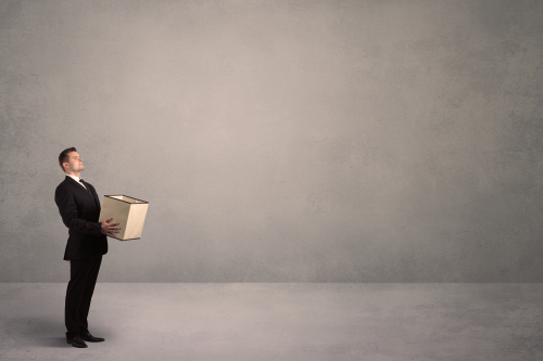 A well dressed young office worker holding an empty paper box with clear concrete wall background concept.