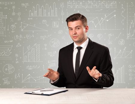 Young handsome businessman sitting at a desk with white graphs and calculations behind him 